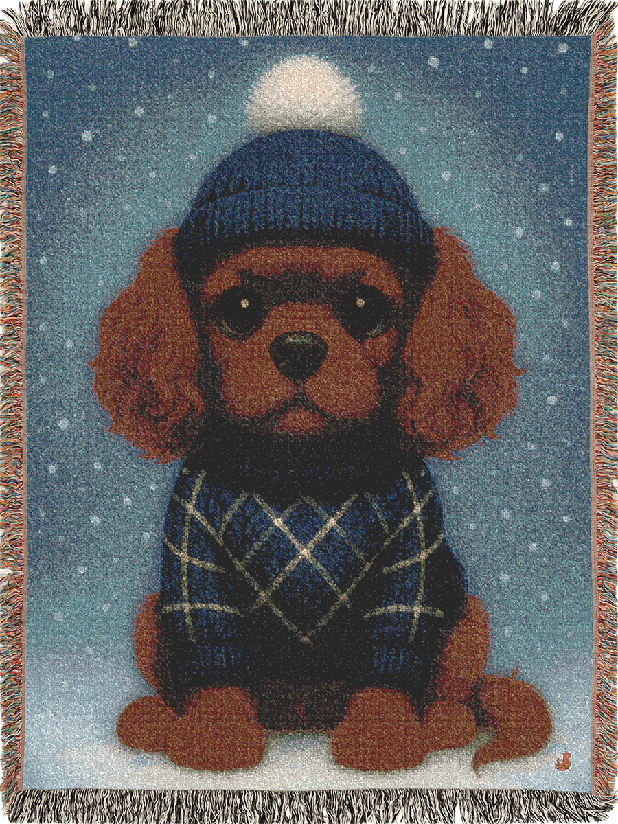 Cavy Comfort woven throw blanket, front view with fringed edges, Ruby Cavalier King Charles Spaniel puppy in a knit beanie and sweater in the snow